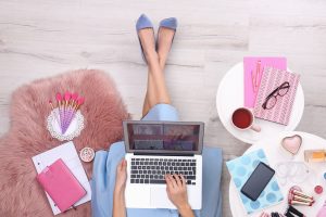 Beauty blogger with laptop and cosmetics sitting on floor, top view