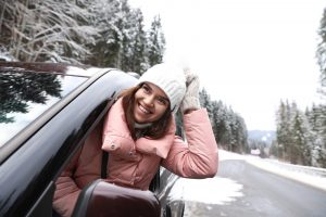 Young woman looking out of car window on road. Winter vacation