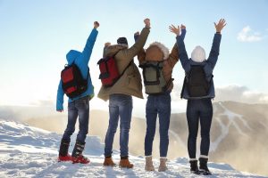 Group of excited friends with backpacks enjoying mountain view during winter vacation