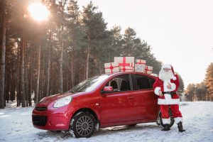 Authentic Santa Claus near red car with gift boxes, outdoors