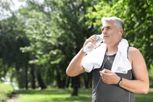Handsome mature man with bottle of water in park, space for text. Healthy lifestyle