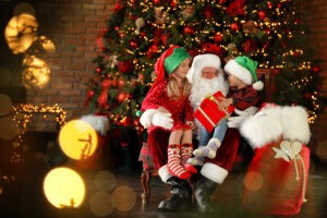 Santa Claus and little children with present near Christmas tree indoors