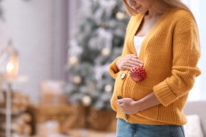 Young pregnant woman with Christmas decoration at home, closeup. Space for text