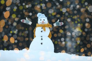 Adorable smiling snowman and blurred Christmas lights on background outdoors. Winter day