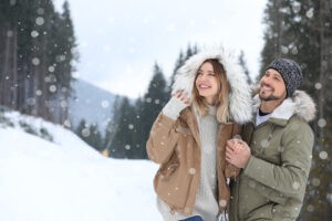 Happy couple near conifer forest on snowy day, space for text. Winter vacation
